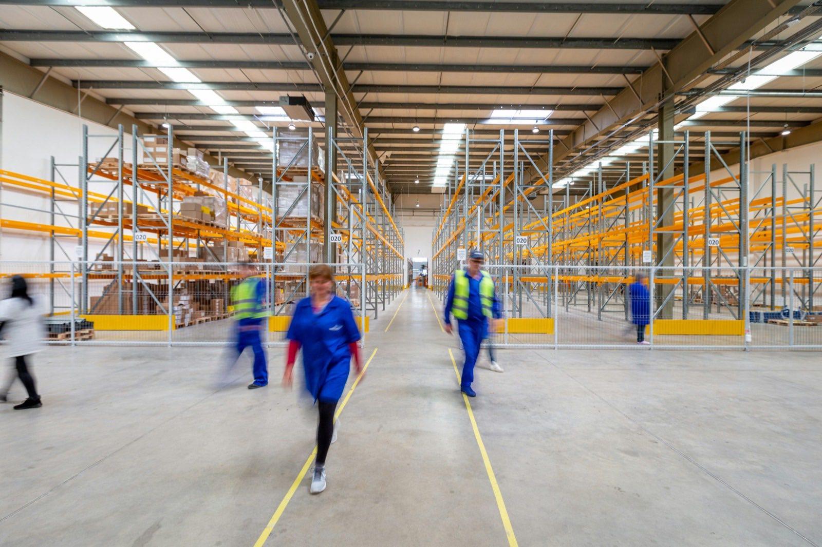 Warehouse workers in hi-vis walking between racking aisles, the kind of site where toolbox talks run